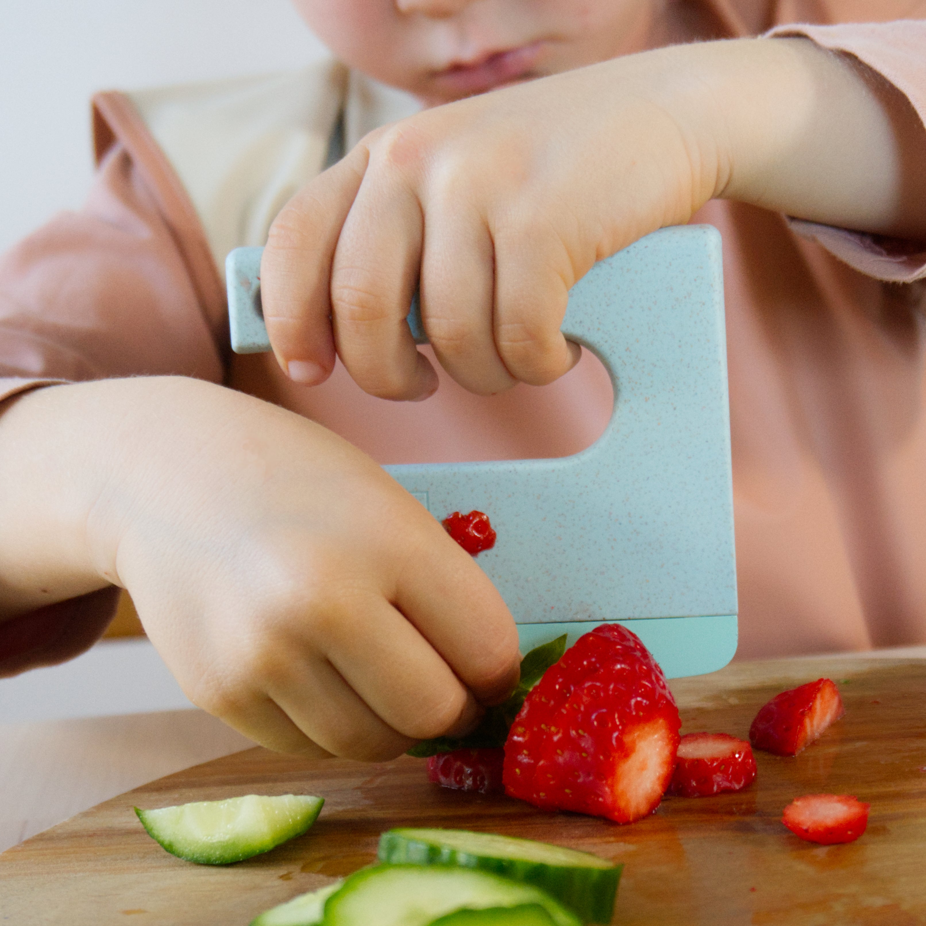 Child cutting strawberries on a wooden cutting board with a safe knife