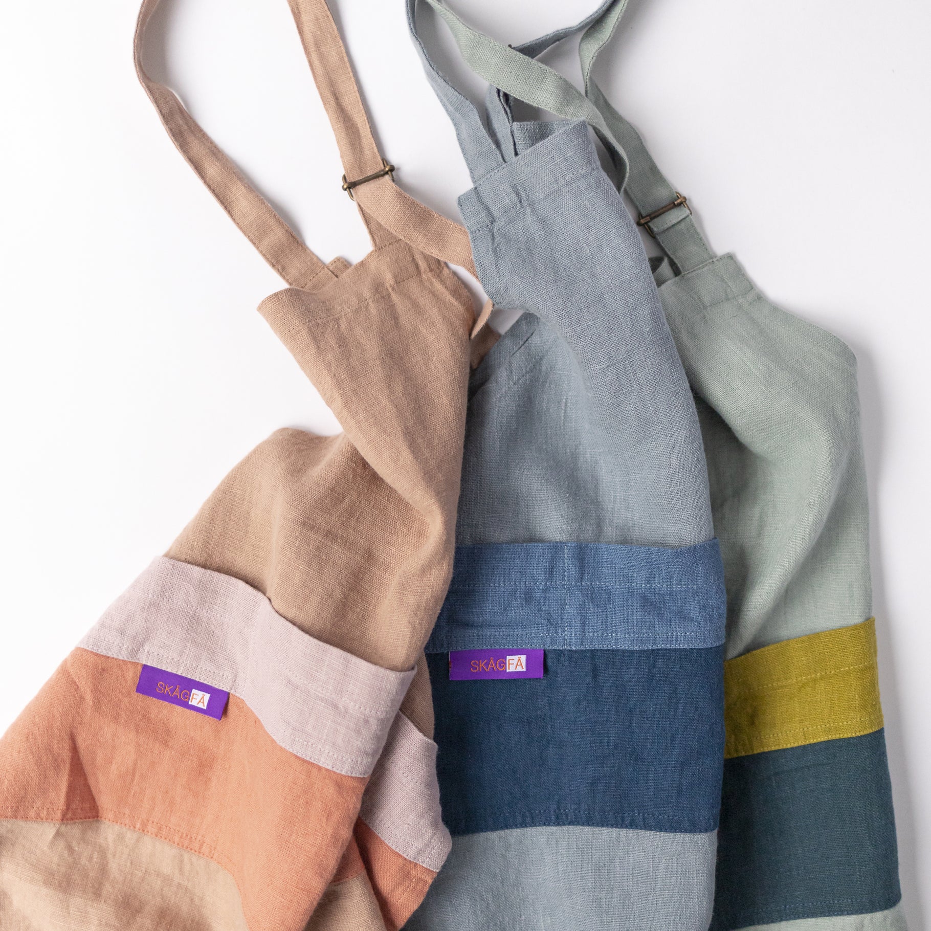 Child in a kitchen wearing 'The Förkläde' linen chef apron by SKÅGFÄ, showcasing adjustable neck strap and deep pockets, designed in Spain and handmade in Europe, perfect for culinary adventures. The apron features chic simplicity with 100% OEKO-TEX certified stone-washed linen, promoting sustainable fashion and functionality for young chefs blue navy pink peach salmon sage green forest