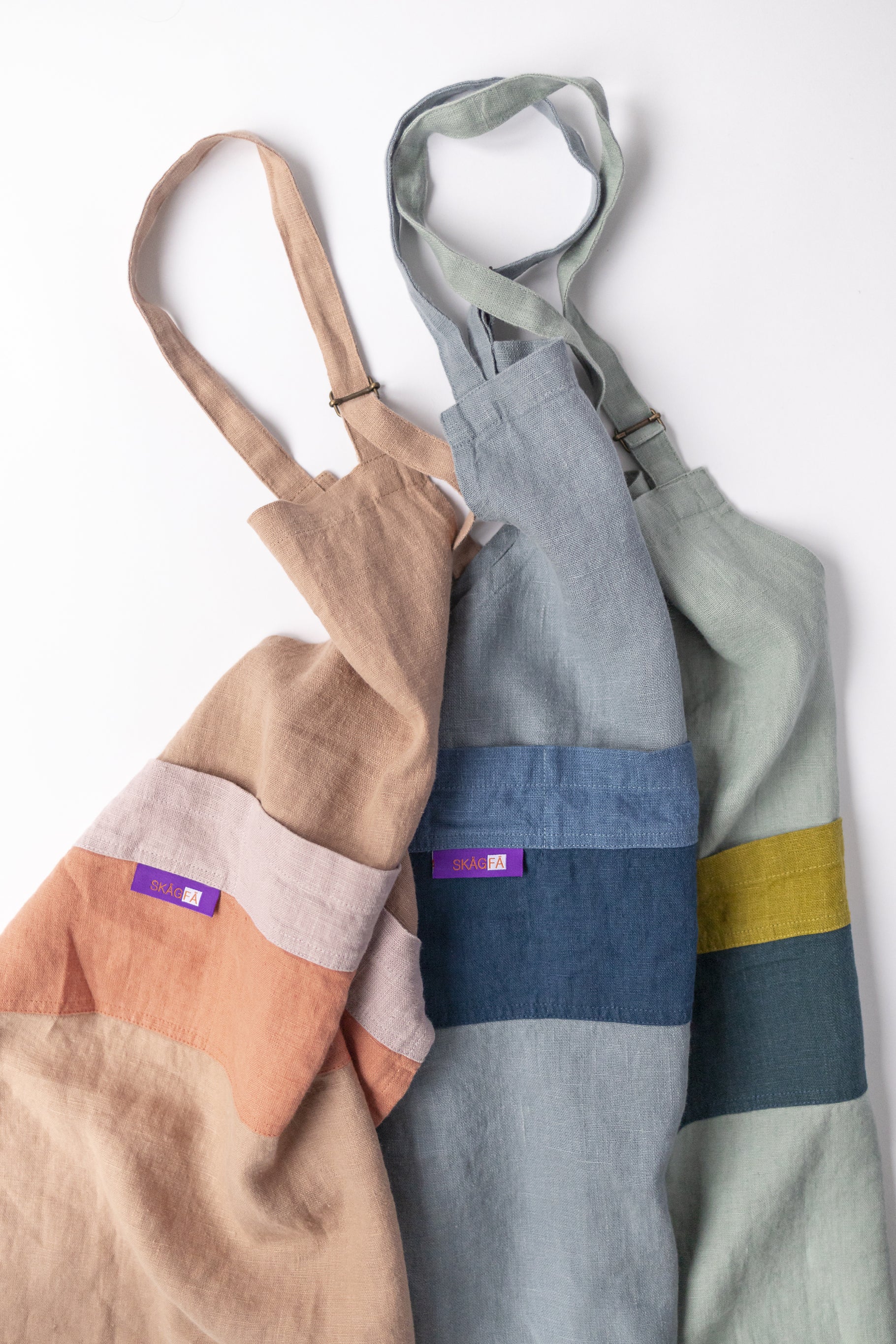 Child in a kitchen wearing 'The Förkläde' linen chef apron by SKÅGFÄ, showcasing adjustable neck strap and deep pockets, designed in Spain and handmade in Europe, perfect for culinary adventures. The apron features chic simplicity with 100% OEKO-TEX certified stone-washed linen, promoting sustainable fashion and functionality for young chefs blue navy pink peach salmon sage green forest