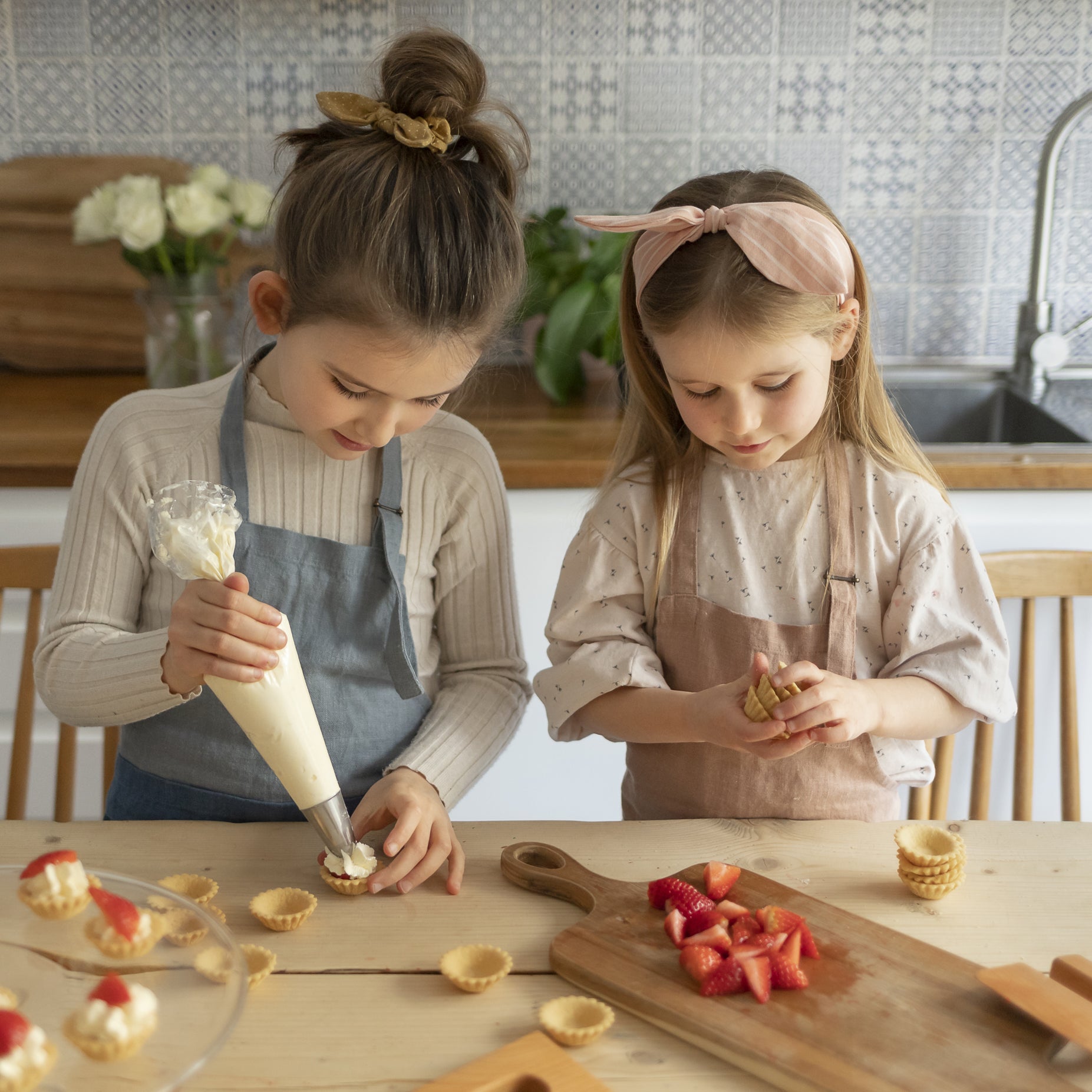 Child in a kitchen wearing 'The Förkläde' linen chef apron by SKÅGFÄ, showcasing adjustable neck strap and deep pockets, designed in Spain and handmade in Europe, perfect for culinary adventures. The apron features chic simplicity with 100% OEKO-TEX certified stone-washed linen, promoting sustainable fashion and functionality for young chefs blue navy pink peach salmon sage green forest. strawberries