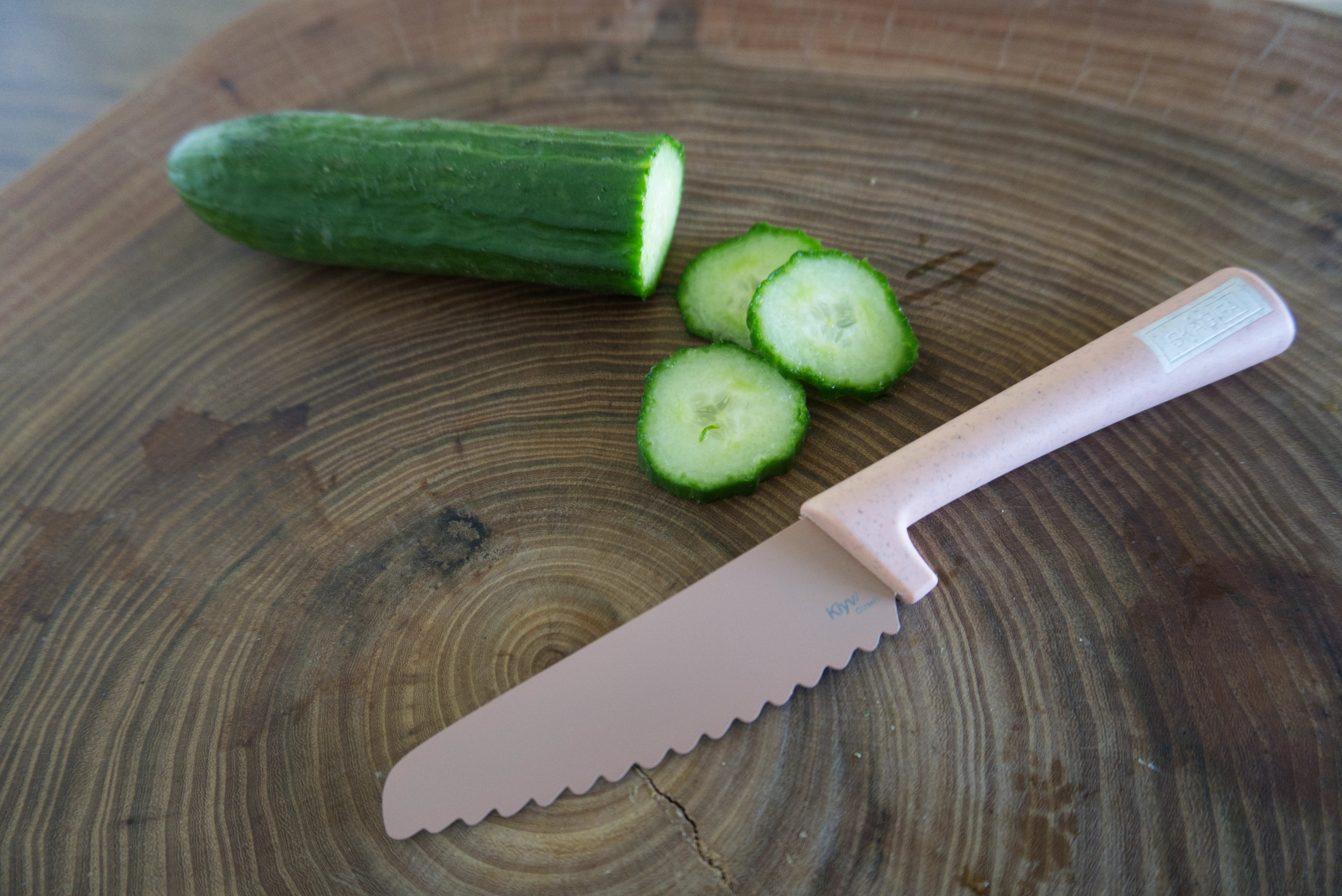 Sliced cucumber on a wooden cutting board with a pink safe knife for kids .