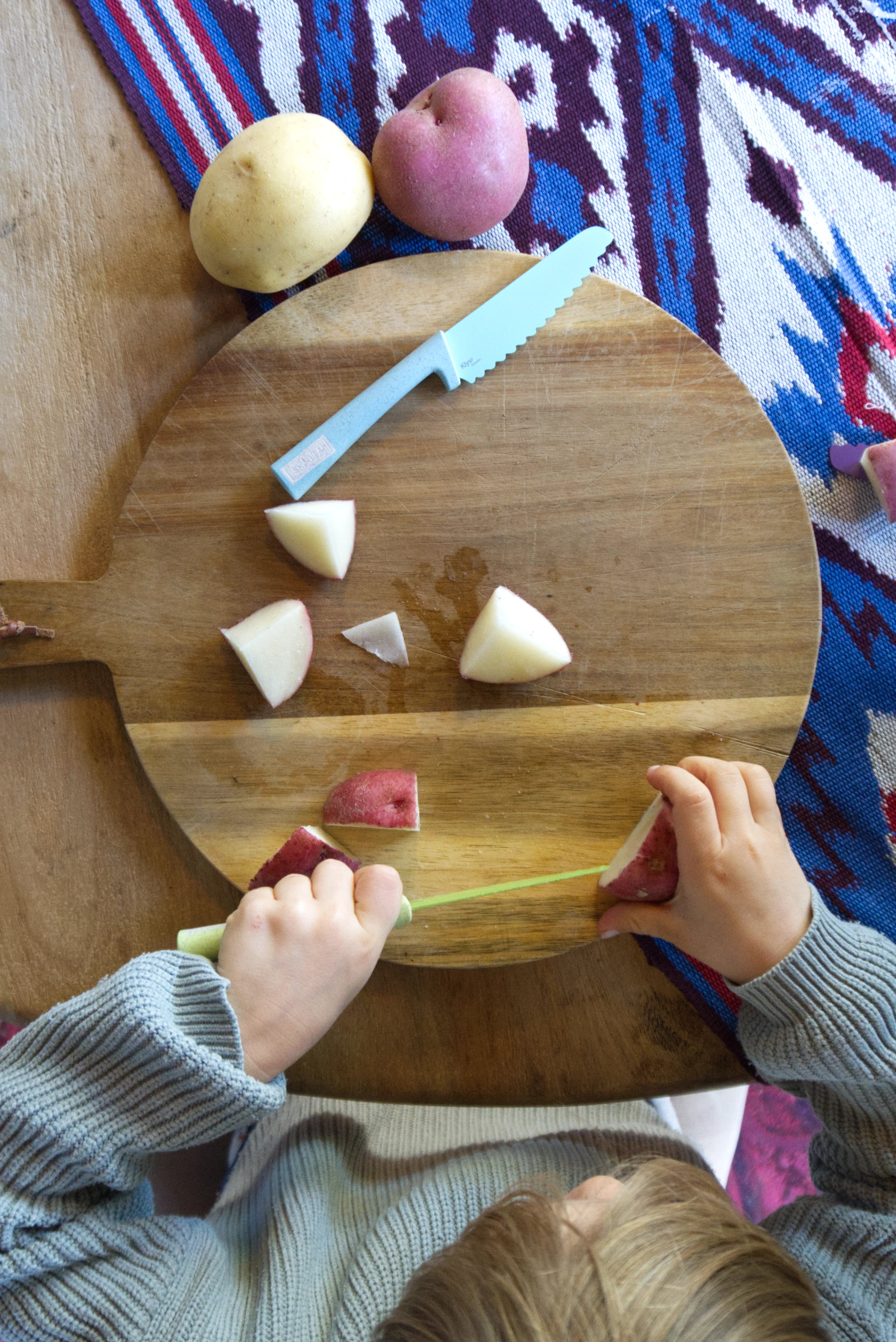 Children's hands peeling potatoes on a wooden cutting board with a knife and peels. Klyv classic knife for 3 years old Scandinavian Design
