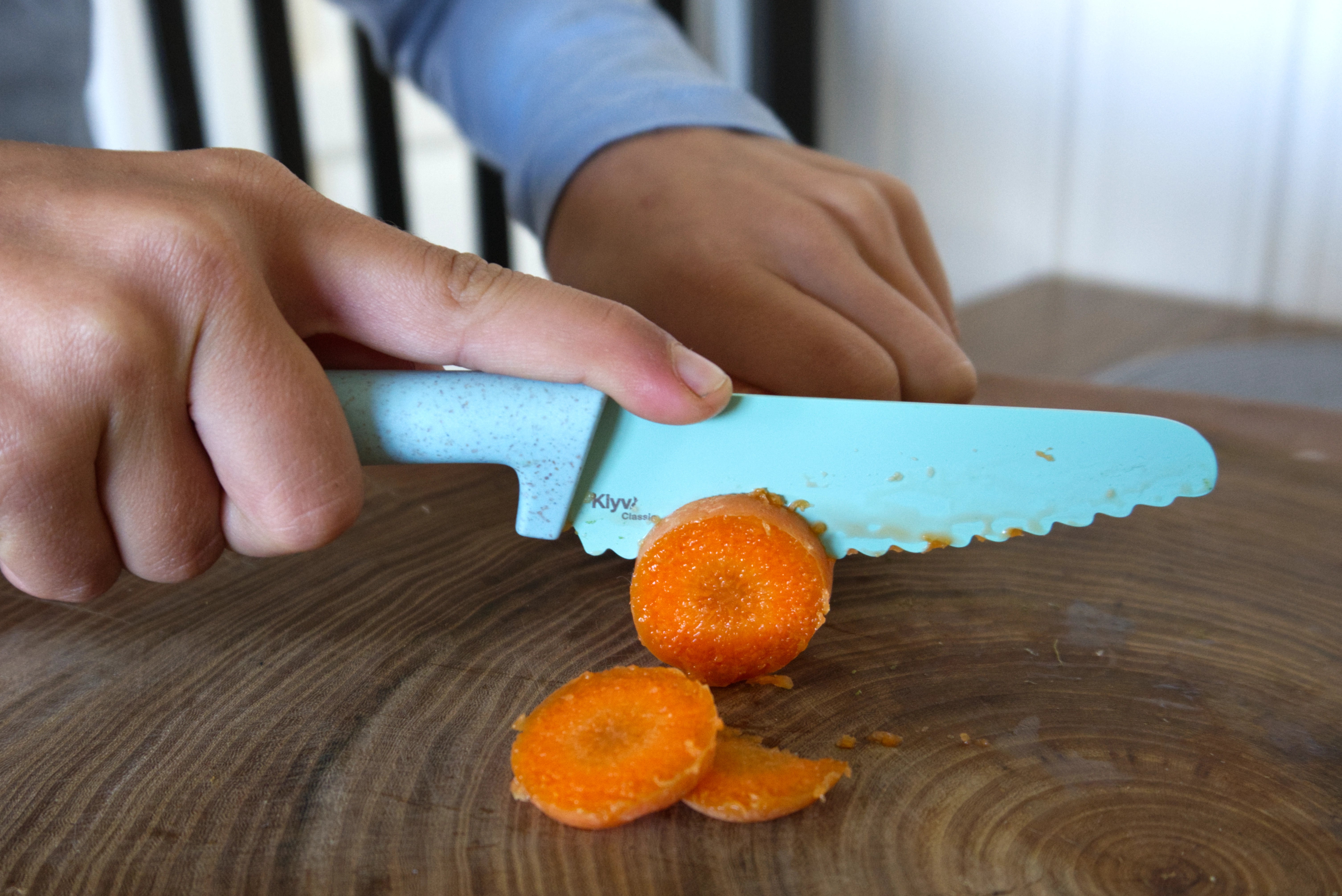 kid cutting carrots with a learning knife on a wooden surface, Klyv classic safe knife for 3 years old Scandinavian Design