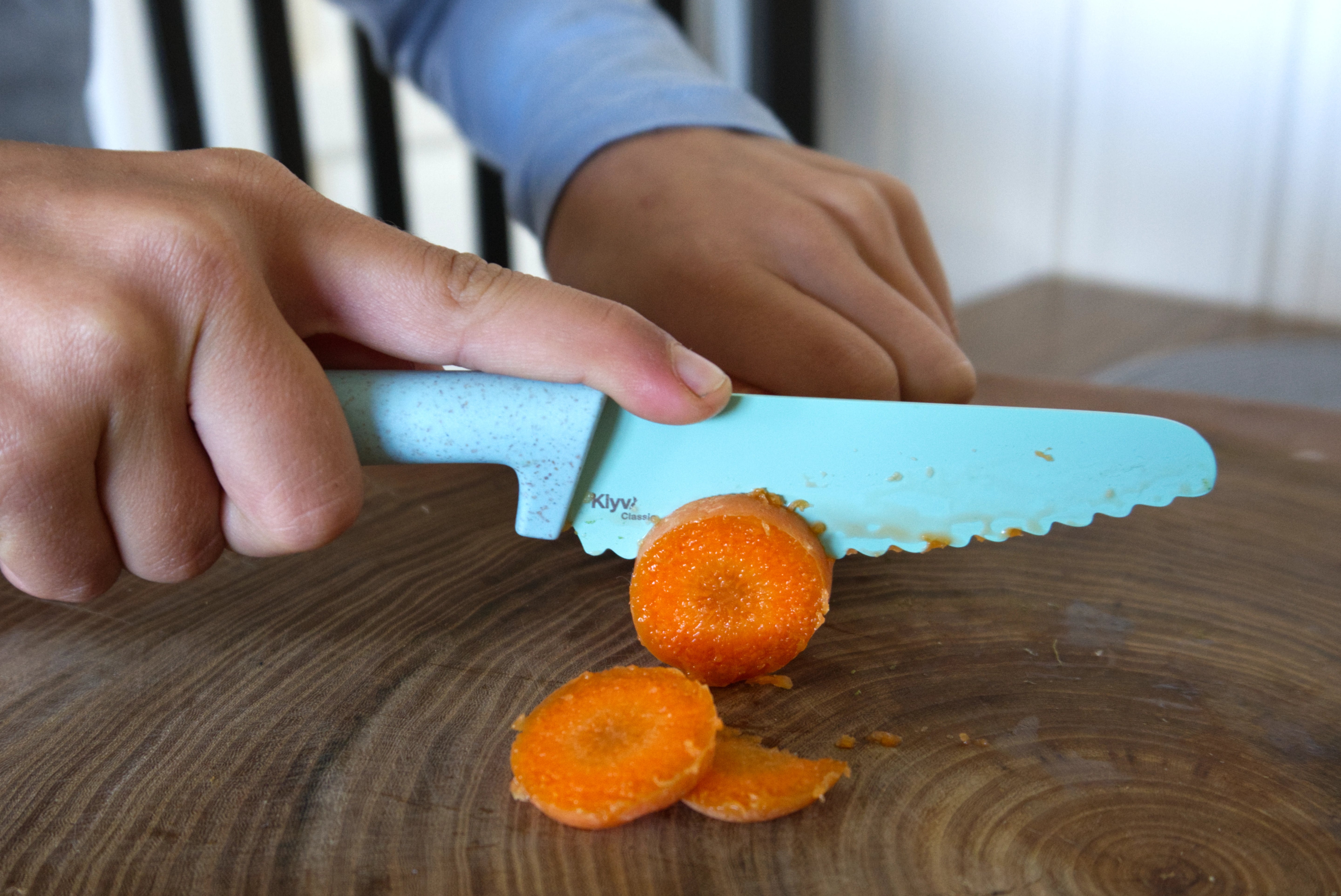 kid cutting carrots with a learning knife on a wooden surface, Klyv classic safe knife for 3 years old Scandinavian Design