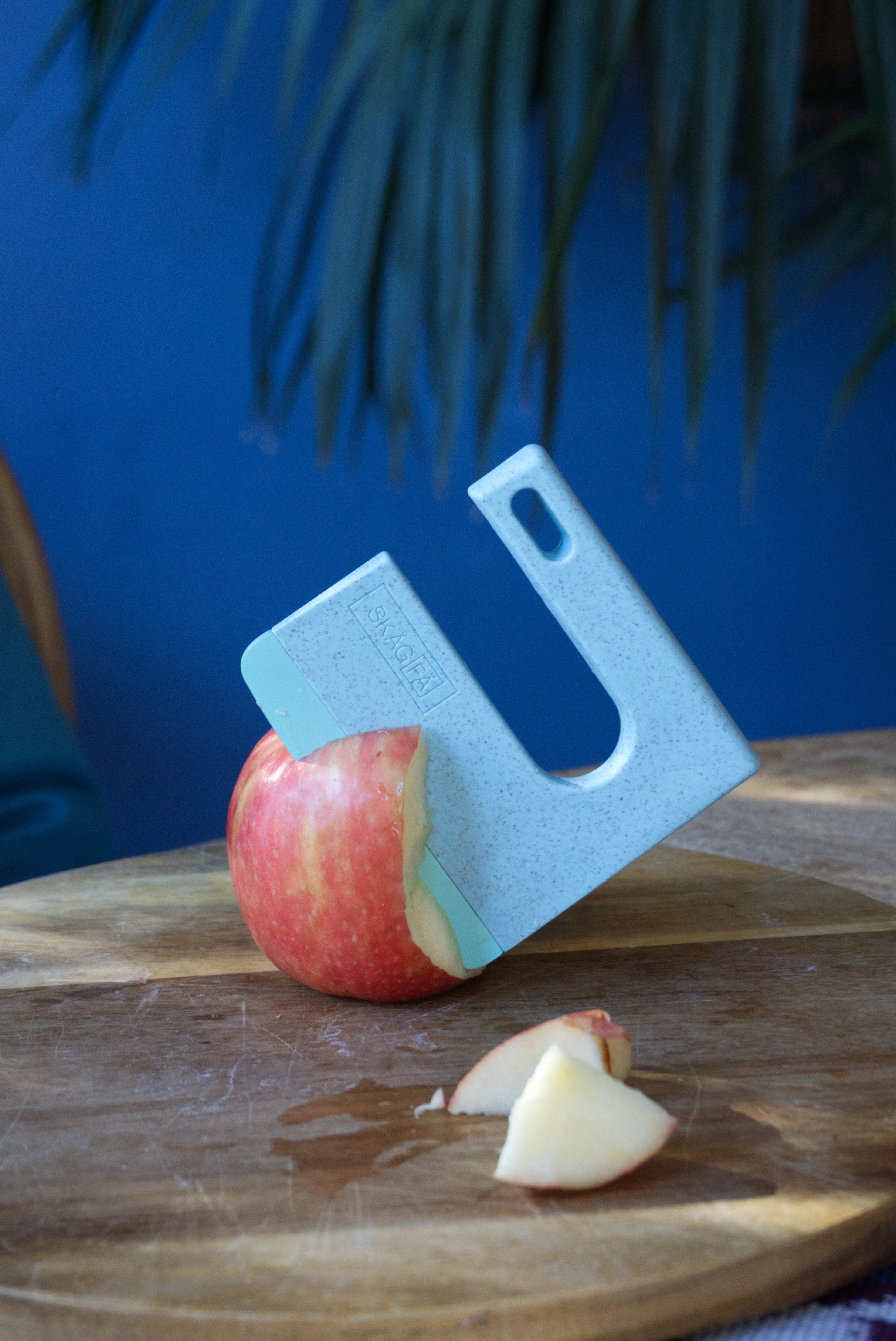 Blue cutting board with a sliced apple on a wooden surface against a blue wall. 