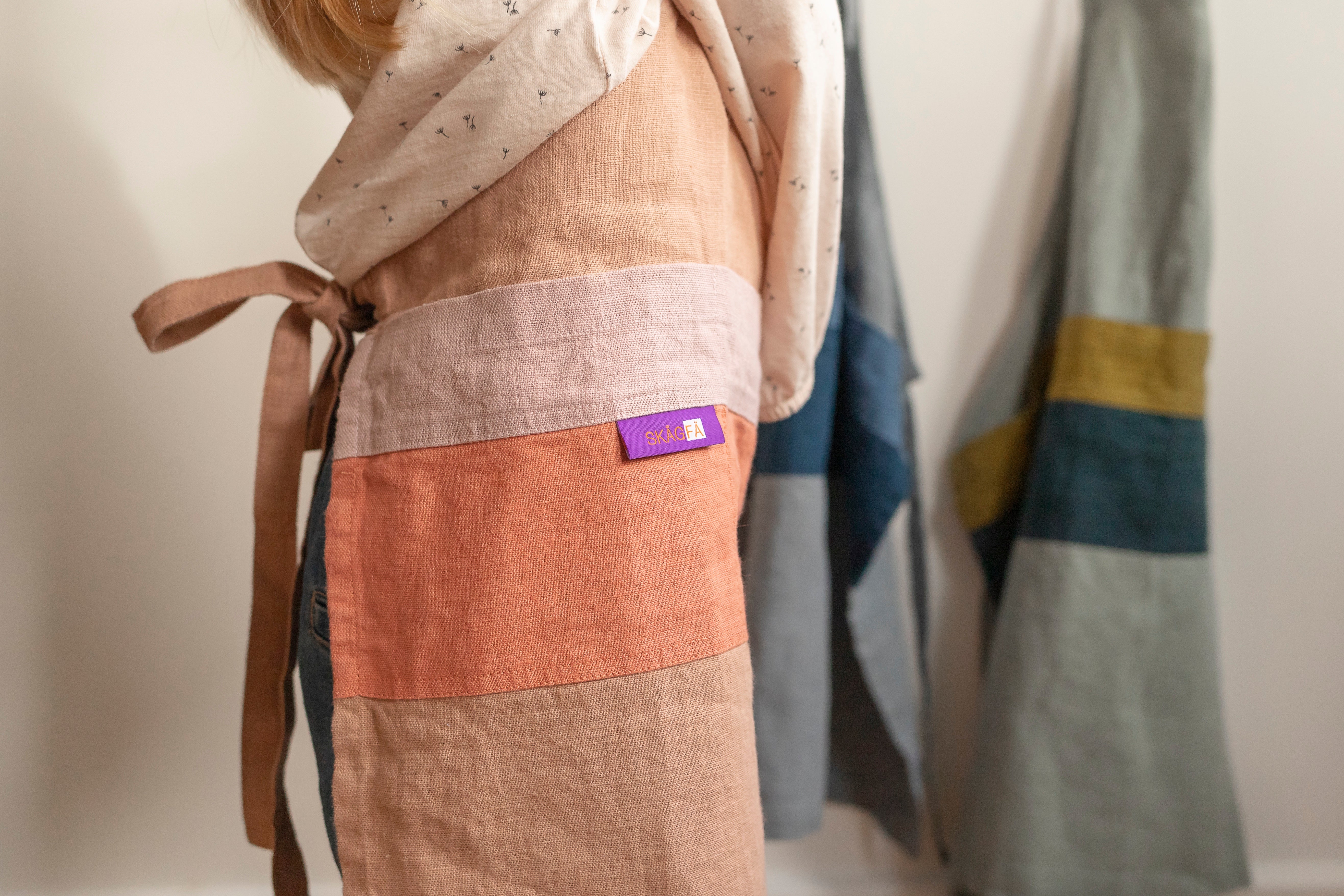 Young chef in a minimalist kitchen sporting 'The Förkläde' linen chef apron by SKÅGFÄ, reflecting Scandinavian design principles with its clean lines and functional features like an adjustable neck strap and deep pockets. Crafted in Europe from 100% OEKO-TEX certified stone-washed linen, this apron combines durability, sustainability, and a timeless aesthetic, ideal for children's culinary explorations.